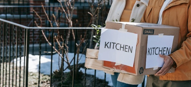 A man is carrying packed kitchen wares in a box.