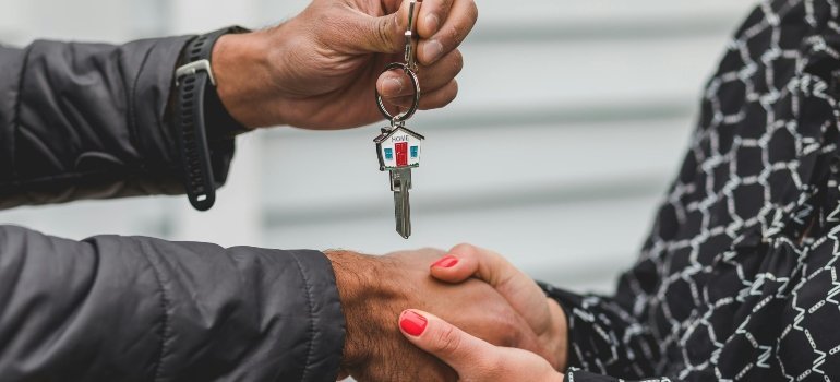 Two people are shaking hands and holding a grey house key.