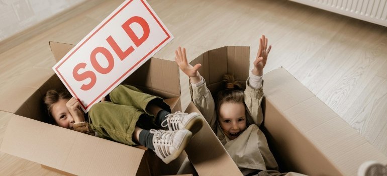 Two kids having fun inside cardboard boxes while celebrating a new home purchase.
