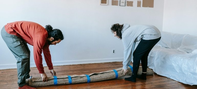 Couple lifting and rolling a carpet while unpacking after Moving from Alexandria to Waldorf.