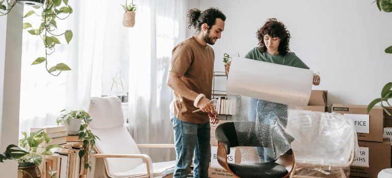 Man and woman preparing furniture with bubble wrap surrounded by packed boxes.