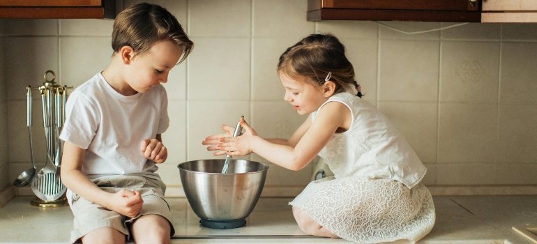 Two children sitting on a kitchen counter mixing ingredients after moving into a new Maryland home.