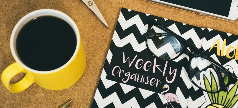 A desk with coffee, planner, and glasses used for scheduling moving plans efficiently.