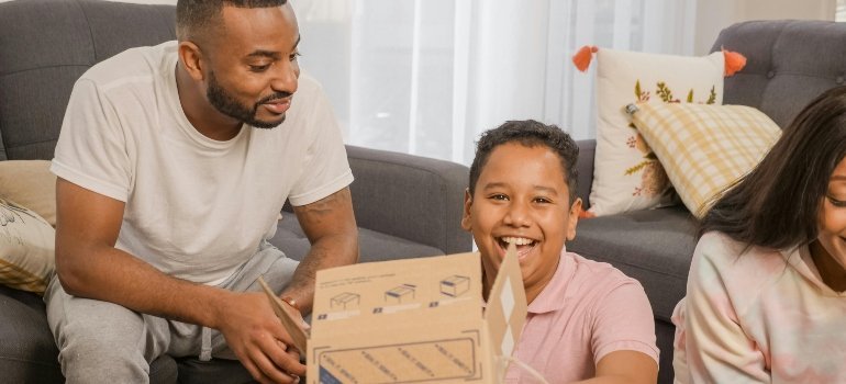 Smiling family packing cardboard boxes while sitting on the floor in their living room.