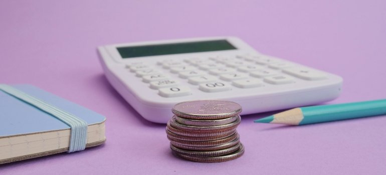 A close-up of stacked coins beside a calculator and notebook symbolizing budgeting and savings.