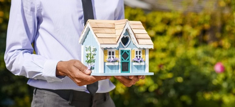 A person holding a miniature house model symbolizing homeownership dreams.