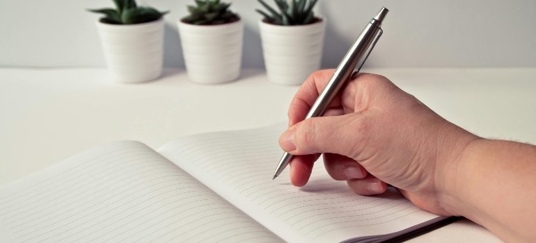A person writing in a notebook while preparing a checklist for their upcoming move.