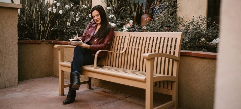 A woman sitting on a bench, writing in a notebook during a calm outdoor moment.
