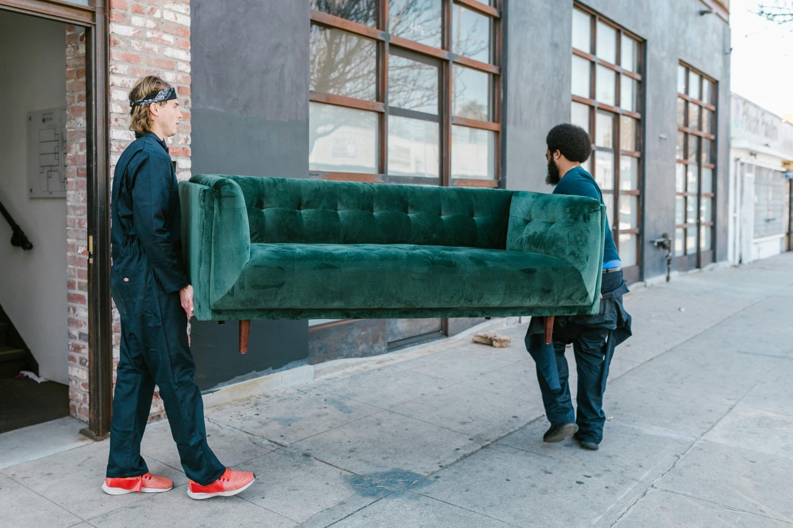 Two movers transporting a green couch outside a building during a Move From New Jersey to Maryland.