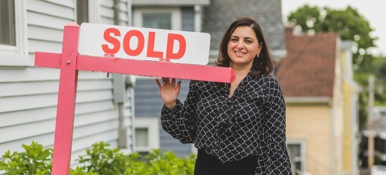 A smiling homeowner standing next to a sold sign, celebrating First-Time Homeowners in Virginia.