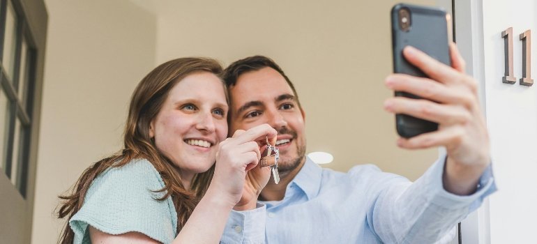 A couple taking a selfie while holding their new house keys in front of their home.