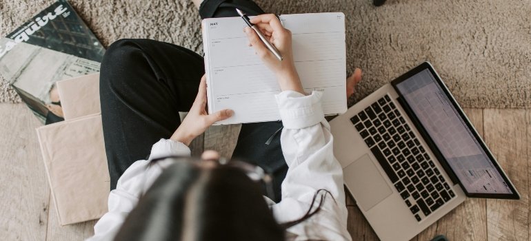 Woman writing in a planner next to a laptop, creating a detailed checklist for her Move Across Virginia.
