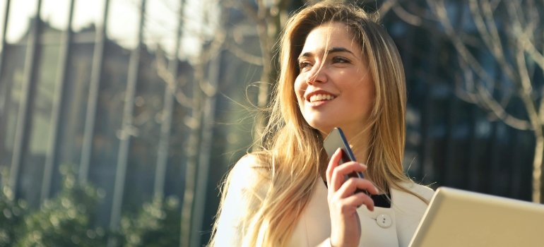 A smiling woman holding a smartphone and tablet.