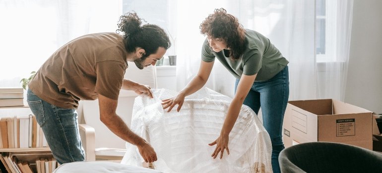 Couple wrapping furniture with bubble wrap while preparing for Long-Distance Moves Out of Maryland.