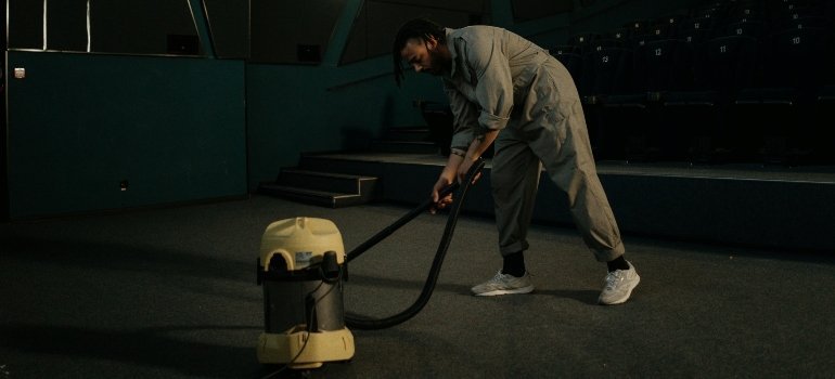 Worker uses a professional vacuum system to clean a wide carpeted space.