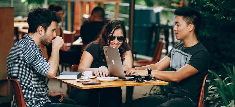 Three people working together on laptops at a café table.