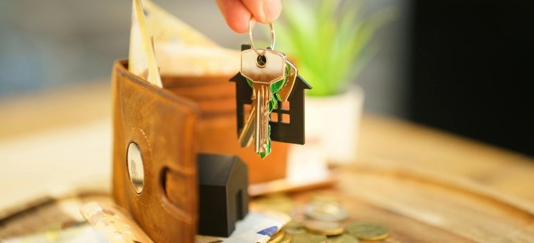 A hand holding house keys above an open wallet, playfully symbolizing buying investment property in Maryland.