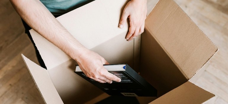 Hands placing a book carefully into a moving box during home packing preparations.