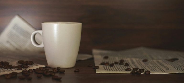Coffee cup with scattered beans and newspapers symbolizing a short pause during moving preparations.