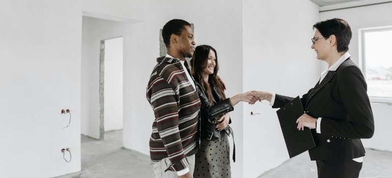 A couple shaking hands with a realtor inside an unfinished home, capturing the excitement of buying investment property in Maryland.