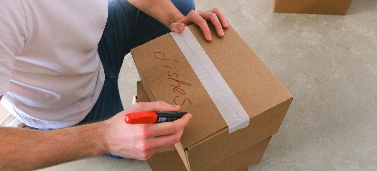 Man labeling boxes “dishes” while preparing kitchen items for Long-Distance Moves Out of Maryland.