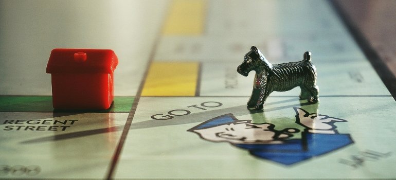 A tiny Monopoly dog figure staring down a plastic house on the game board, ready to make its move.