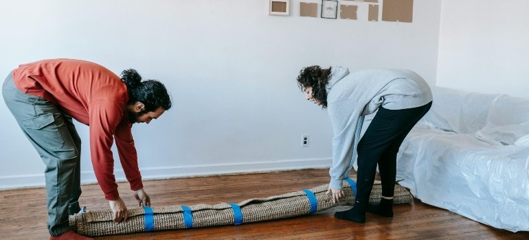 Couple lifting a rolled carpet while settling in and learning how to feel at home when moving to Annapolis