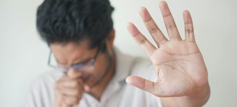 Selective focus photo of a coughing man’s hand, illustrating the risk to health when you catch a cold while moving house