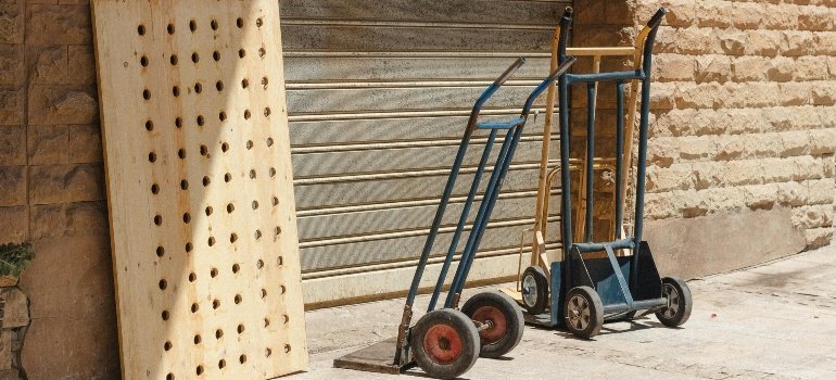 Best equipment for moving heavy furniture including hand trucks and a wooden panel placed against a brick wall