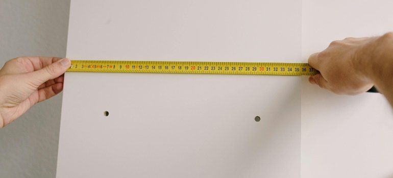 Crop man measuring wooden board in room