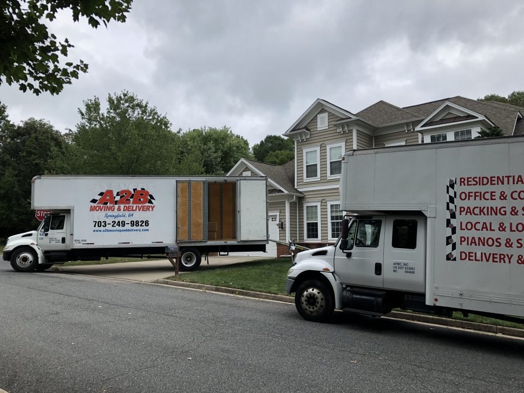 Two moving trucks parked in front of a beige suburban house.
