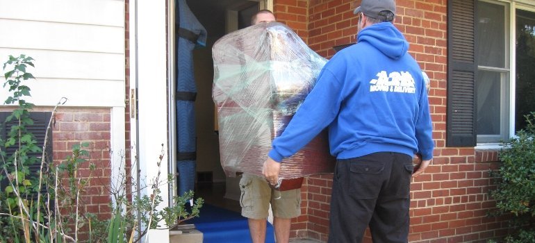 Movers carrying wrapped furniture out of house during relocation.
