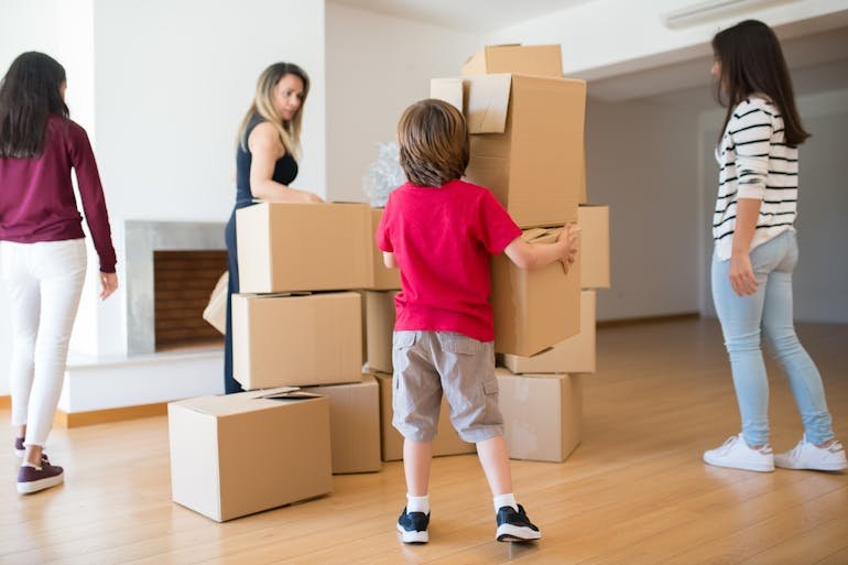 Family carrying and stacking cardboard boxes in an empty room, illustrating involving teenagers in the moving process during a home move.