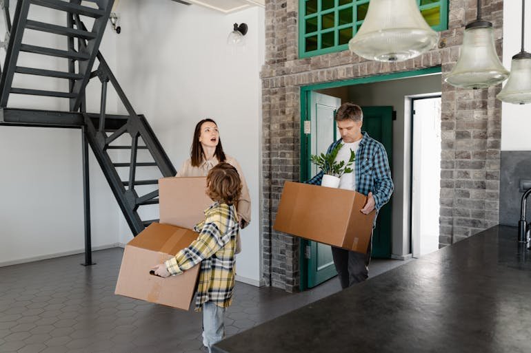 Family carrying cardboard boxes into a new home, illustrating moving with kids from Falls Church to Sterling and settling in together.