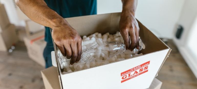 Man using DIY packing tips while packing glasses into a cardboard box.